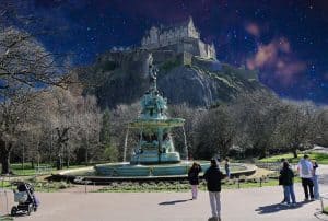 Group of people smiling near the fountain in Princes Street Gardens with Edinburgh Castle in the background.