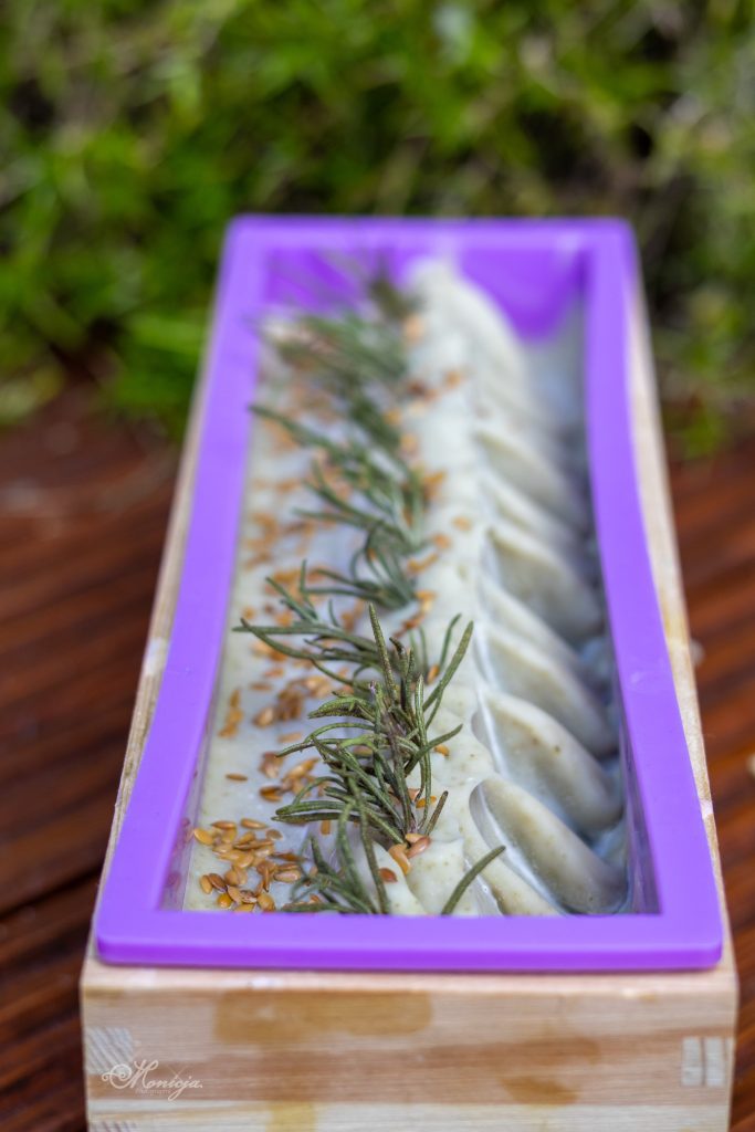 Uncut loaf of cold-process handmade soap in a wooden mold, showing swirled top textures and natural botanical ingredients.