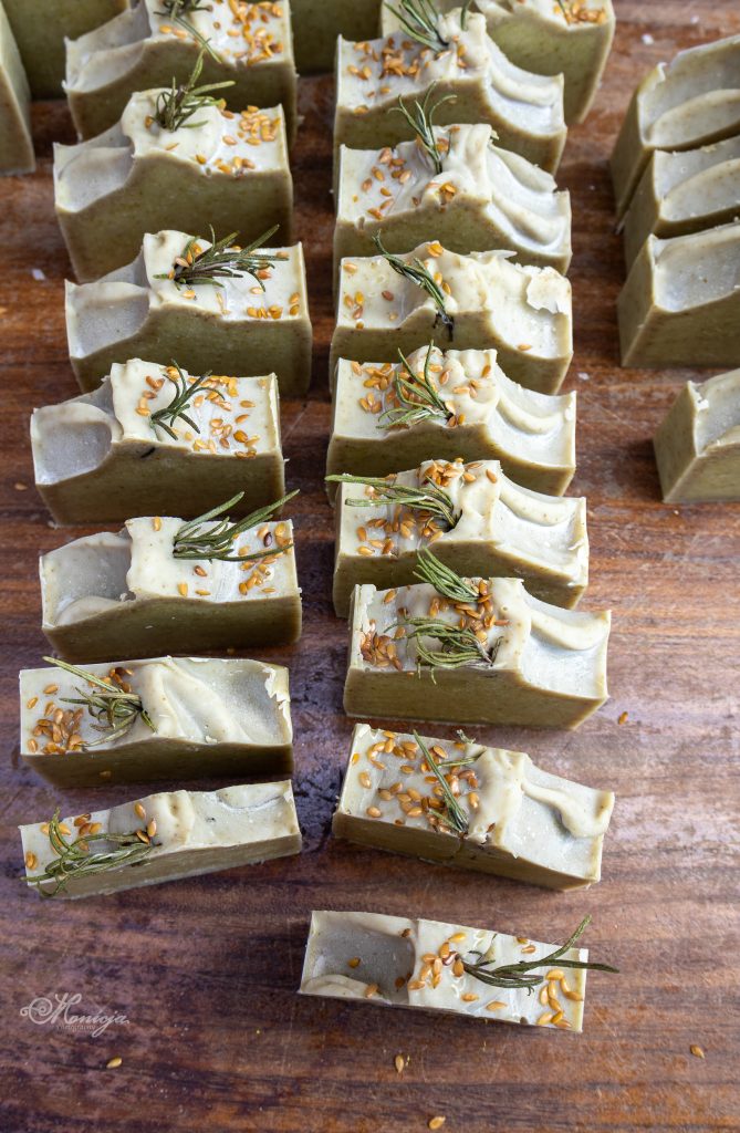 Stack of small‑batch, organic, cold‑process handmade soap bars with botanical swirls on a rustic wooden table