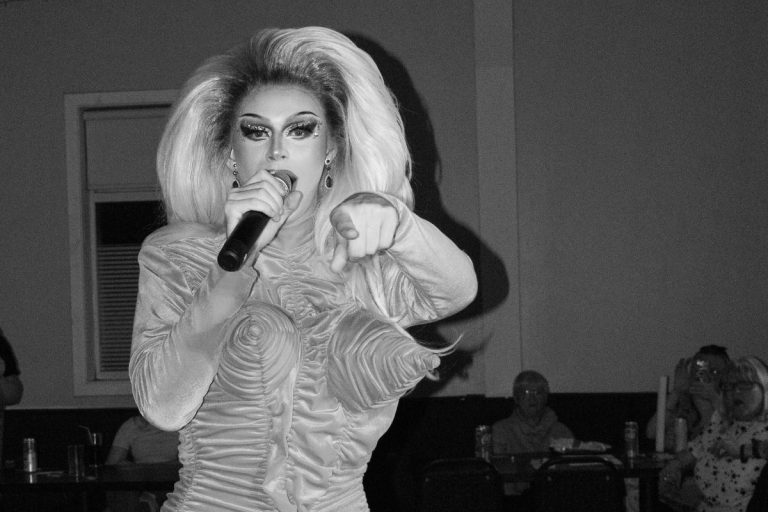 Drag queen in glamorous dress singing and pointing to the audience during live performance.