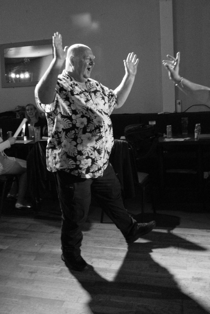 Black and white photo of an audience member dancing with raised arms during Penicuik charity night.