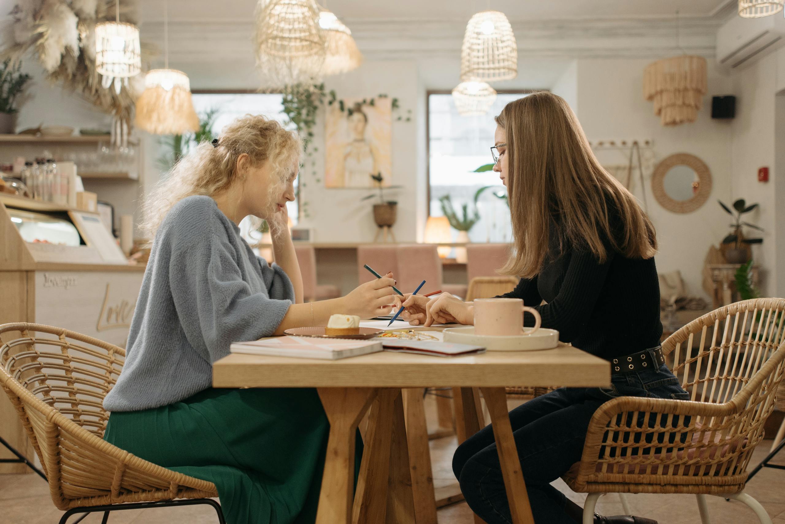 Two women collaborating and writing in a cozy cafe setting over coffee and pastries.