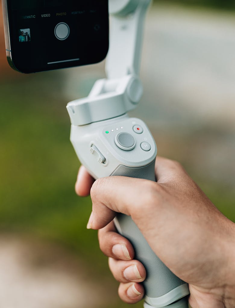 Photo by I'm Zion A close-up view of a hand holding a smartphone stabilizer outdoors, ideal for filming.