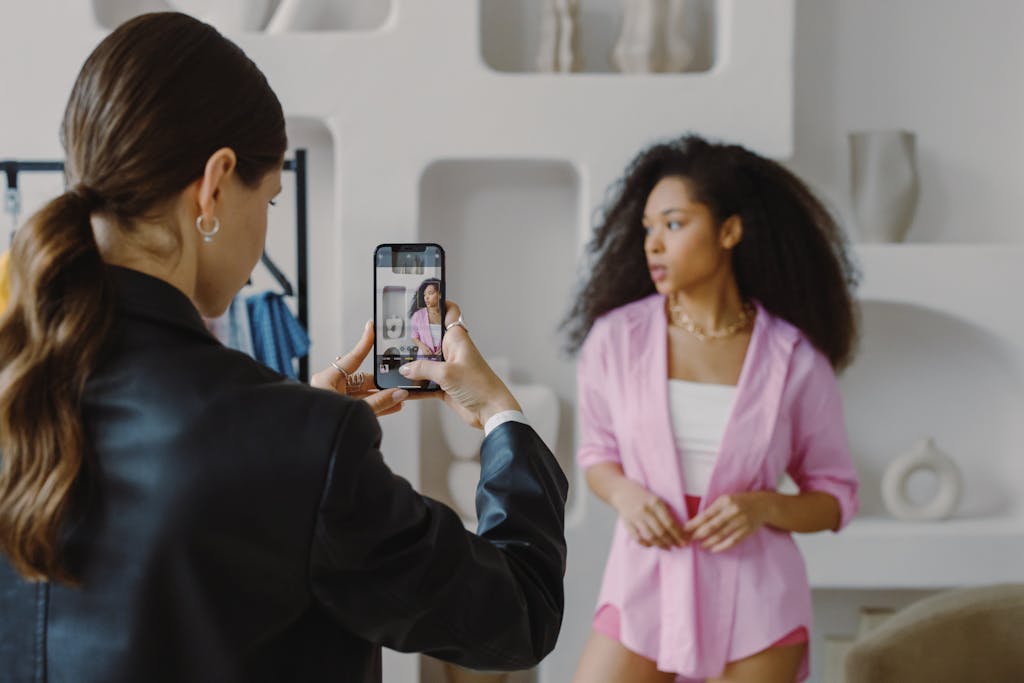A woman uses a smartphone to photograph a model posing indoors. Modern and creative.