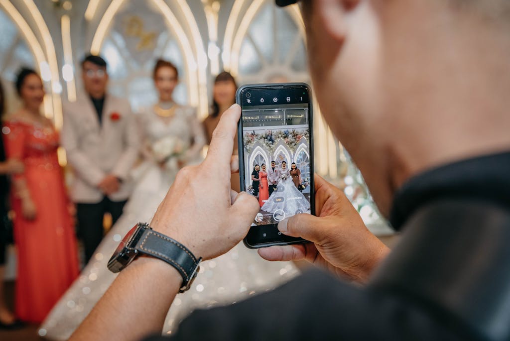 Close-up of a man photographing a wedding scene on a smartphone.